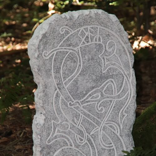 Cette image représente une pierre tombale grise dans la forêt. On peut voir dessus un dragon avec des runes nordique, Algiz à l'envers, Othalan et Ansuz. 